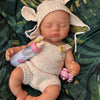 A hand-painted silicone reborn doll with pink ears and a light pink knitted outfit lying on green fabric.