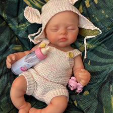A hand-painted silicone reborn doll with pink ears and a light pink knitted outfit lying on green fabric.