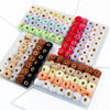A collection of 35 plush fur pom pom beads in various colors and shades arranged in small plastic trays for jewelry making