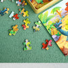 A collection of wooden animal and vehicle jigsaw puzzle pieces scattered on a green surface next to a yellow puzzle box.