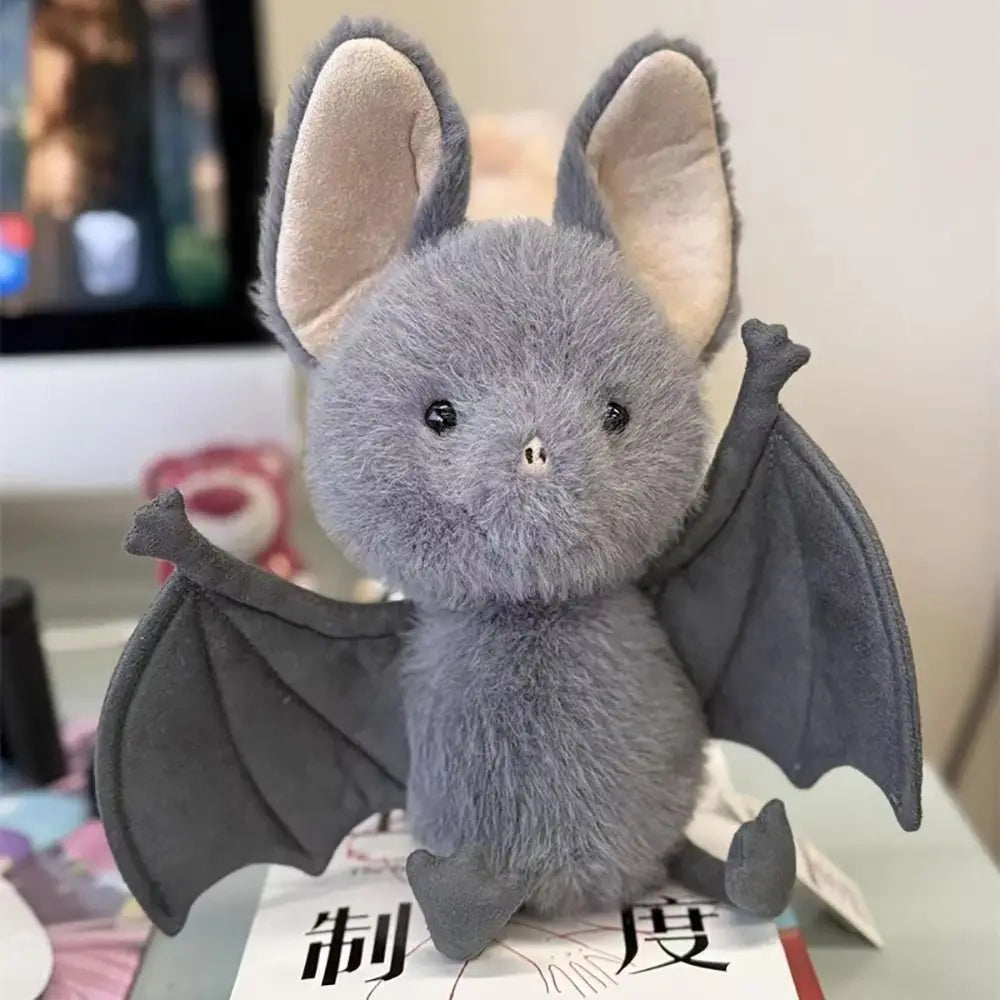 A soft grey bat plush toy with large ears and dark wings is shown against a light background.