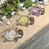 A collection of glow-in-the-dark mini sea turtle figurines in various colors resting on a light surface with moss and small s