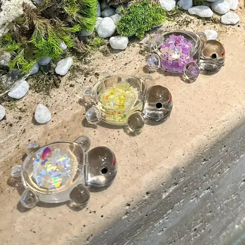 A collection of glow-in-the-dark mini sea turtle figurines in various colors resting on a light surface with moss and small s