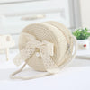 A beige handwoven straw crossbody bag featuring a delicate white lace bow and pearl detail.