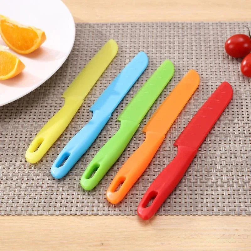 A set of five colorful plastic kid-friendly safety knives arranged diagonally on a woven mat.