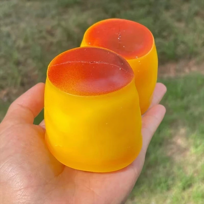A hand holds a bright orange and yellow caramel pudding stress ball with a smooth, squishy texture.