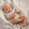A lifelike vinyl reborn doll with a green outfit lying on a cream-colored knitted fabric.