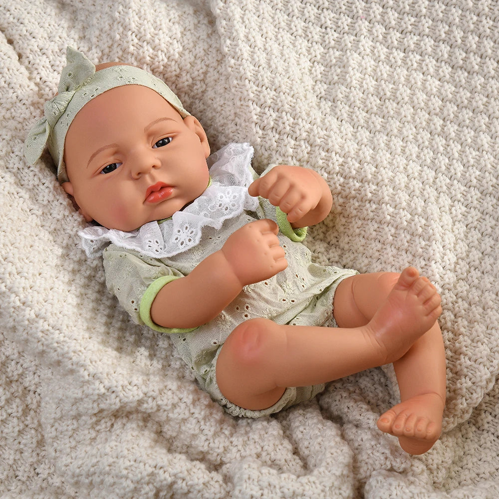 A lifelike vinyl reborn doll with a green outfit lying on a cream-colored knitted fabric.