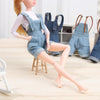 A mini doll wearing denim overalls and a white shirt, with several other similar outfits in the background.