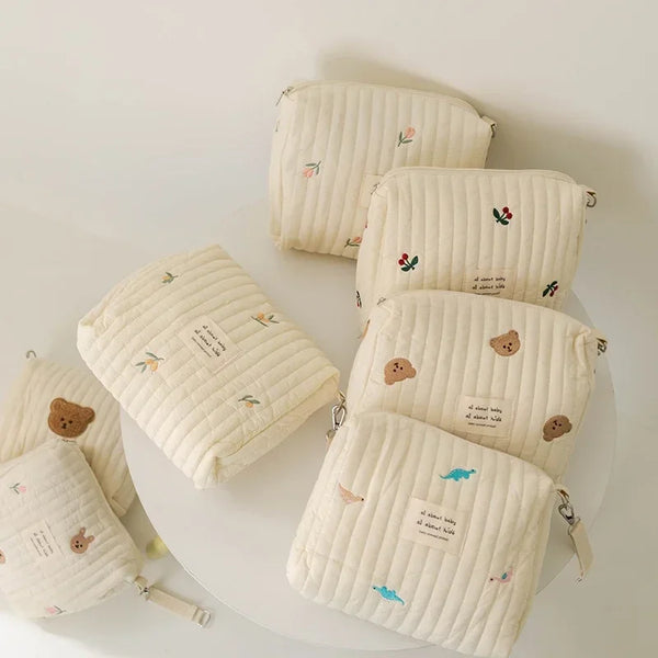 A collection of cream-colored quilted cotton diaper and organizer bags are displayed on a white surface.