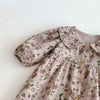 A close-up of a floral doll collar baby girl long sleeve jumpsuit in beige fabric.
