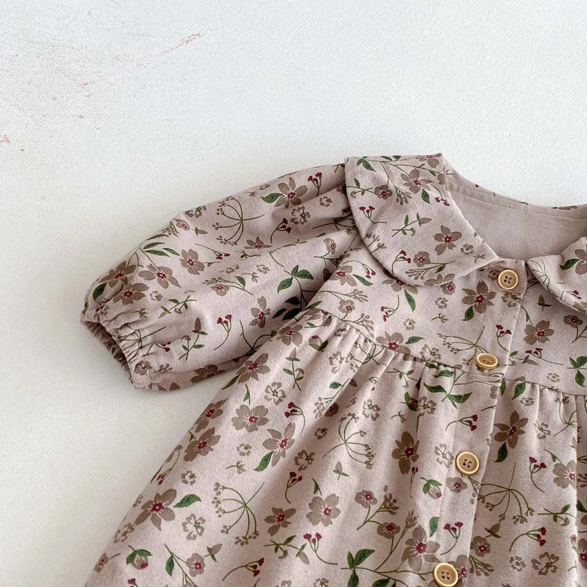 A close-up of a floral doll collar baby girl long sleeve jumpsuit in beige fabric.