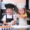 Two children wearing chef aprons and hats are preparing food on a counter.