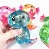 A hand holds a blue glitter axolotl squishy toy next to two other colorful axolotl toys.