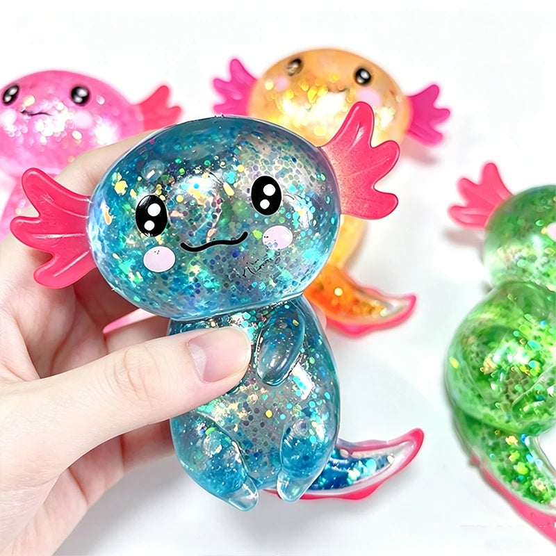 A hand holds a blue glitter axolotl squishy toy next to two other colorful axolotl toys.