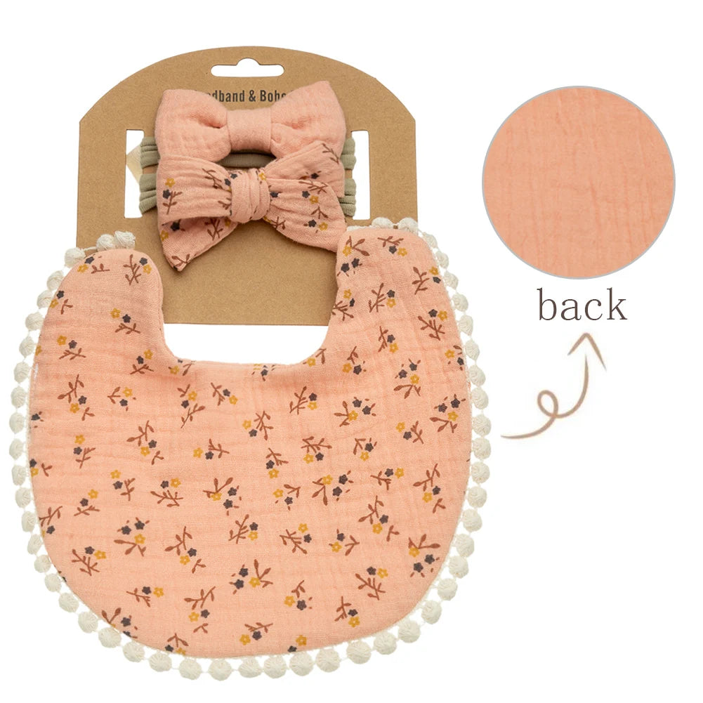 A pink floral baby bib and headband set with a bow, presented on a brown card.