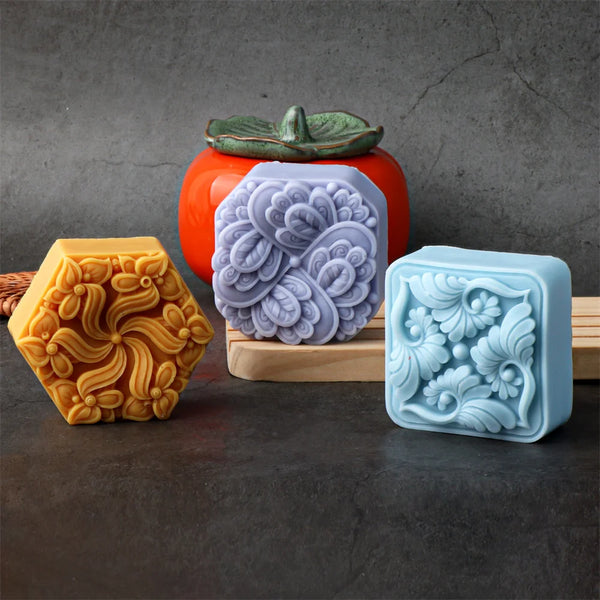 Three silicone flower molds in yellow, purple, and blue are displayed on a dark surface next to an orange pot.
