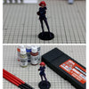 A female figure in a dark blue outfit with red hair is displayed on a black base, next to a set of water-based paint colors.
