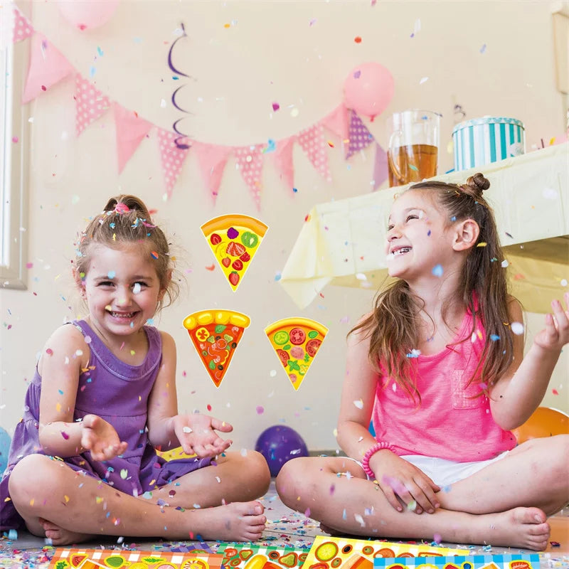 Two young girls laughing while crafting pizza stickers on a table with colorful confetti and balloons.