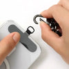 A hand is attaching a black detachable lanyard strap to the edge of a white phone case.