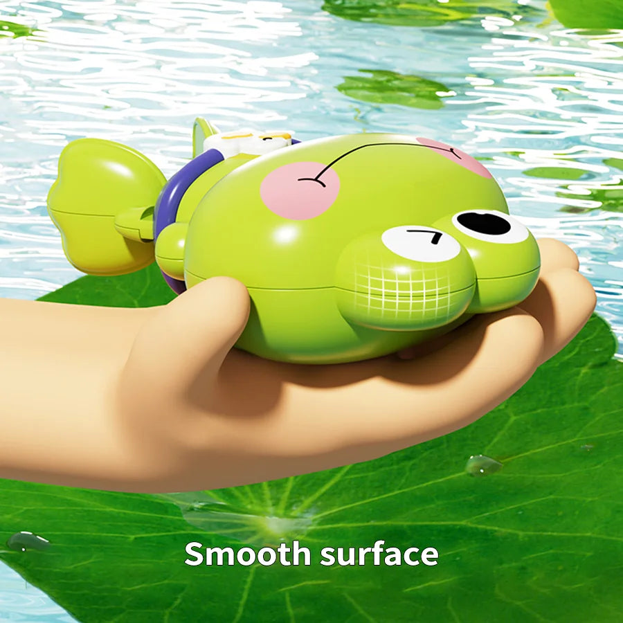 A hand is holding a green floating frog bath toy set on a green leaf surface.