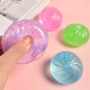 A hand holds a purple glitter squishy bun next to two other colorful glitter stress relief toys.