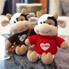 A plush cow stuffed animal with white and brown markings sitting on a dark surface.