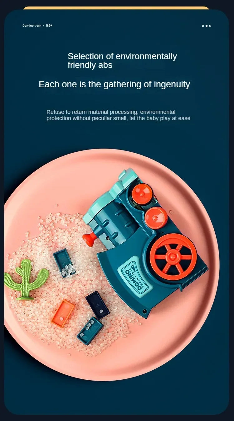 A teal automatic domino train toy is shown resting on a pink plate surrounded by small, light-colored building blocks.