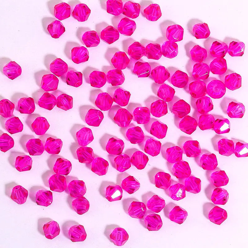 A pile of small, faceted pink crystal bicone glass beads for jewelry making.