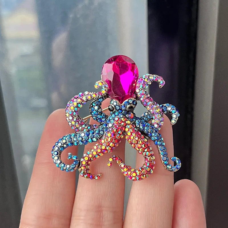 A close-up of a rhinestone turtle brooch pin featuring a pink gemstone and iridescent blue and purple rhinestones.
