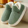 A pair of green knitted slippers with white soles and faux fur lining resting on a light surface.