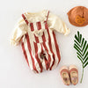 A cream and brown striped baby romper with bear decorations lying next to a tan hat and pink sandals.