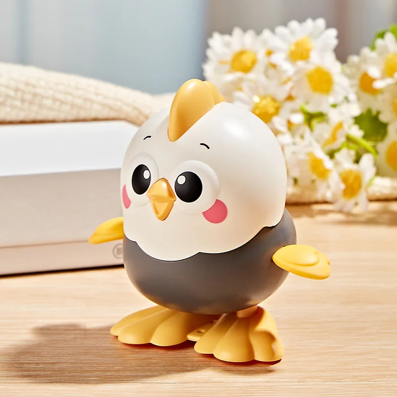 A cute ceramic wind-up chick toy with a yellow beak and gray body sitting on a wooden surface.