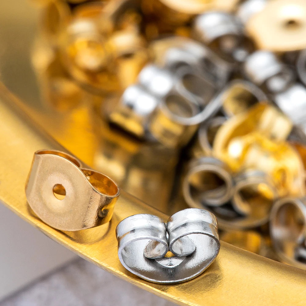 A close-up of stainless steel earring stud bases with backs arranged on a gold surface.