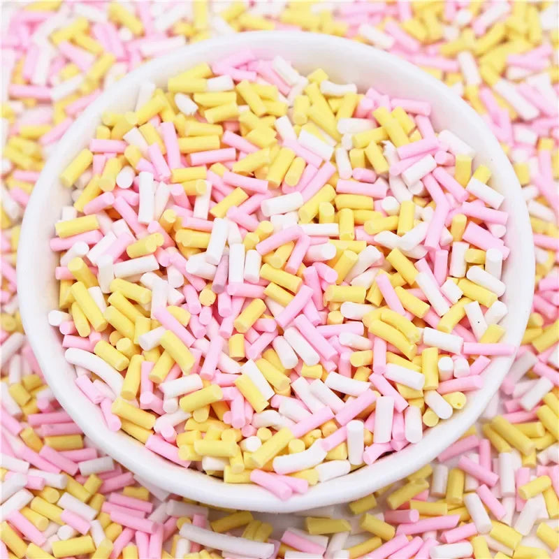 A white bowl filled with colorful polymer clay slice sprinkles in pink and yellow on a pink surface.