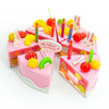 A pink birthday cake with candles and decorations, surrounded by various colorful pretend play items like plastic cutlery and