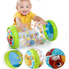 A smiling baby is interacting with a clear plastic crawling roller toy featuring colorful wheels and designs.