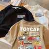 A close-up of a beige crew neck t-shirt featuring a yellow toy car graphic and text encouraging building together.