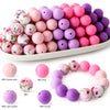 A variety of soft food-grade silicone beads in pink, purple, and white are displayed on a white plate.