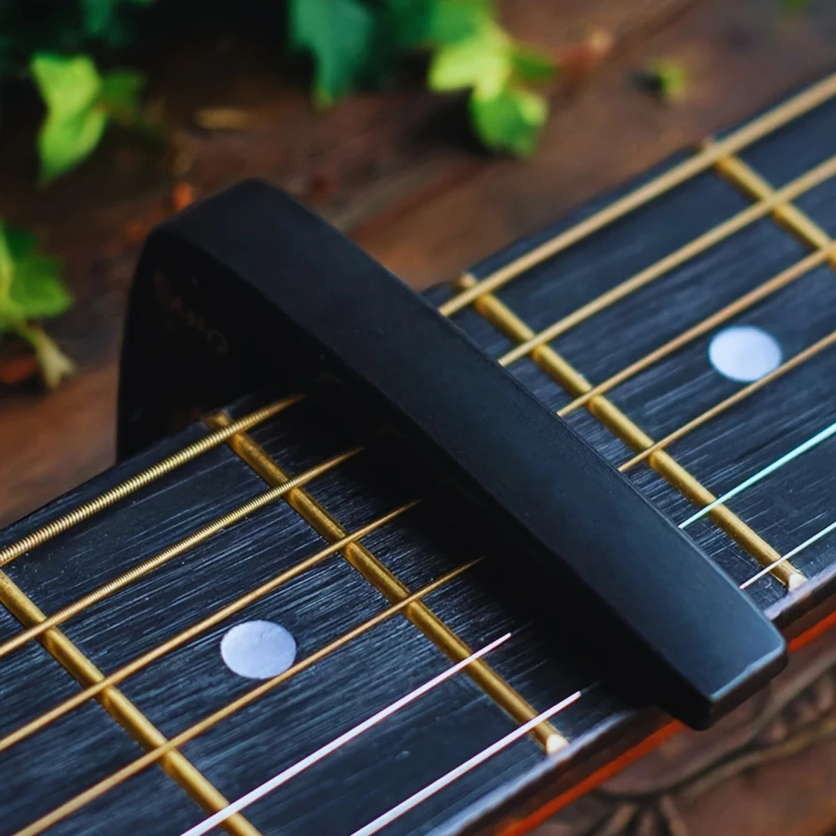 A black aluminum alloy quick-change guitar capo is placed on the fretboard of a dark wood guitar.