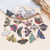 A collection of various butterfly drop charms in gold and silver tones arranged on a light gray surface.