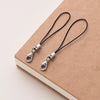A pair of silver lobster clasp keychains with black cord resting on a brown notebook.