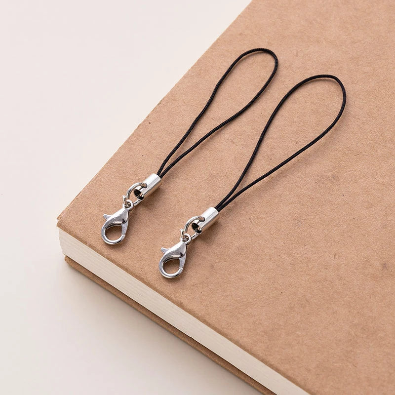 A pair of silver lobster clasp keychains with black cord resting on a brown notebook.