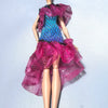 A fashion doll wearing a vibrant pink and blue sheer dress with ruffled sleeves against a light background.