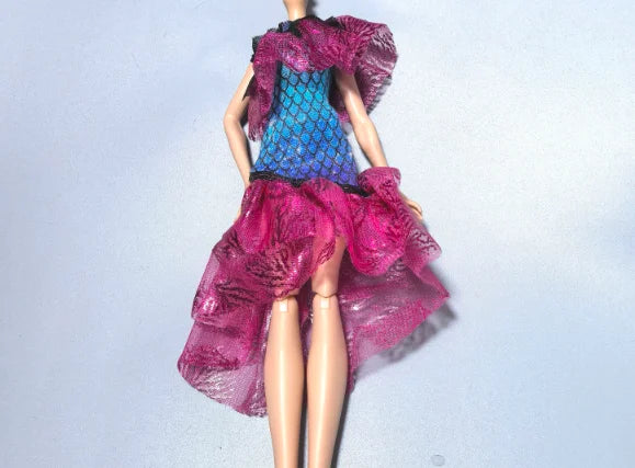 A fashion doll wearing a vibrant pink and blue sheer dress with ruffled sleeves against a light background.