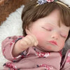 A handcrafted reborn newborn doll with soft silicone body sleeping on a white fluffy surface.
