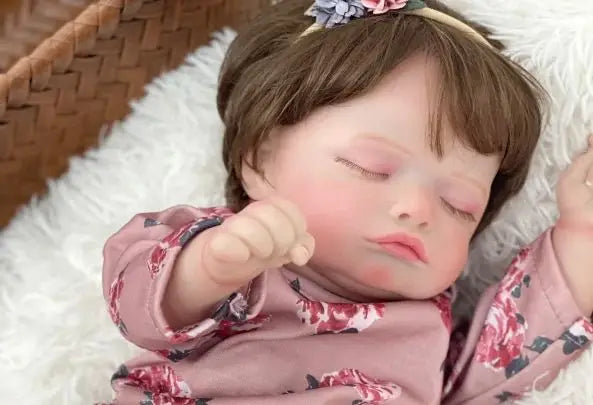 A handcrafted reborn newborn doll with soft silicone body sleeping on a white fluffy surface.