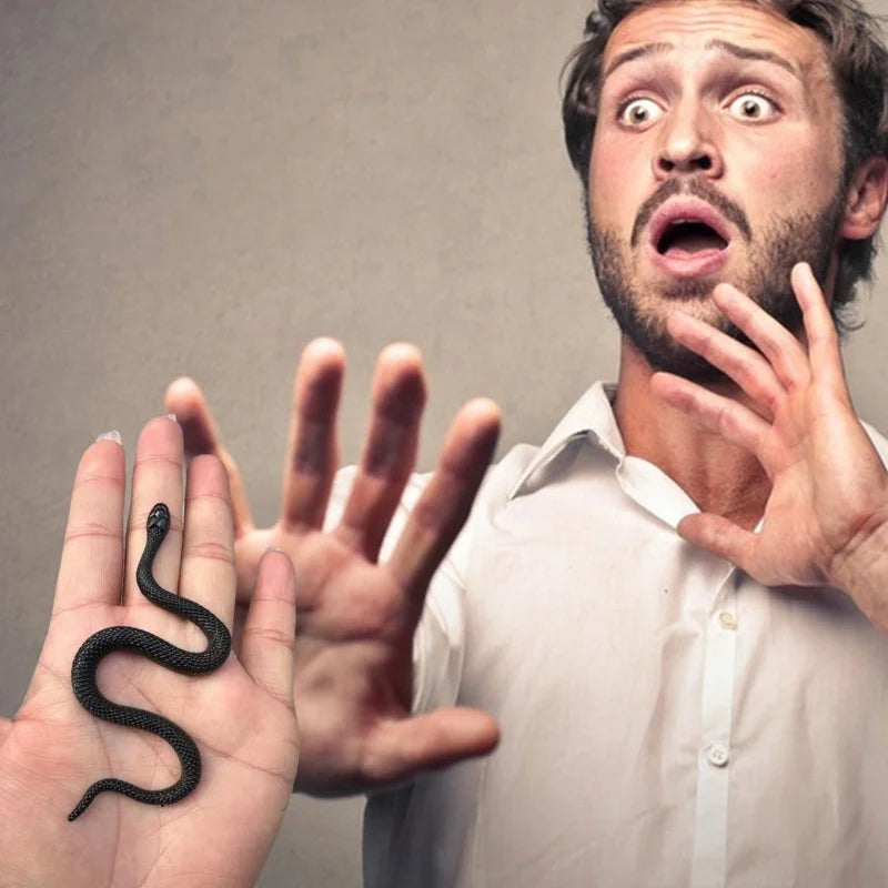 A man's hand shows a realistic soft rubber snake prop, with his face expressing surprise.