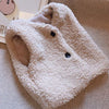 A white, fluffy lamb wool vest with a V-neck and two buttons is displayed on a textured fabric background.
