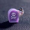 A small purple and white figurine shaped like a pumpkin bear with a skull design.